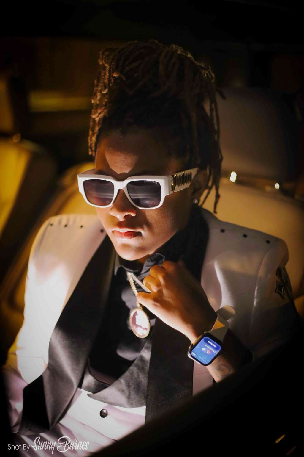 Jayluvv seated in a white suit and white sunglasses